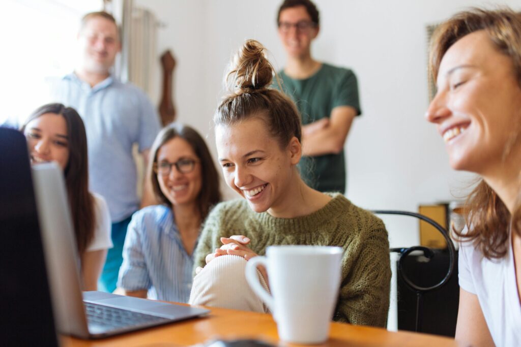 A group of friends enjoying a moment together indoors, smiling and watching a video on a laptop.