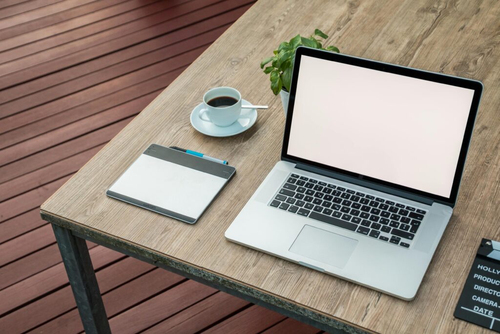 A minimalist outdoor workstation with laptop, coffee, and tablet on a rustic table.