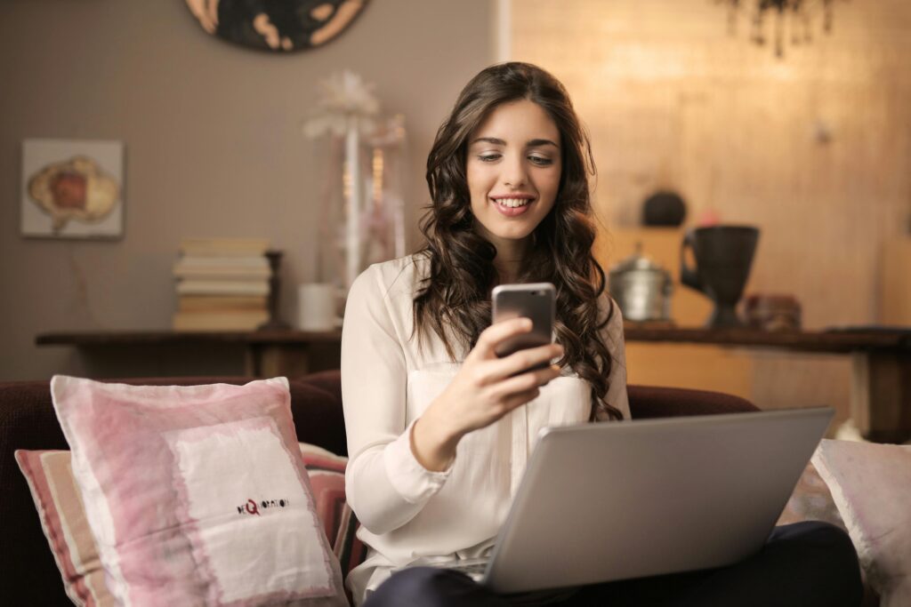 A woman enjoying leisure time using her smartphone and laptop in a cozy living room.